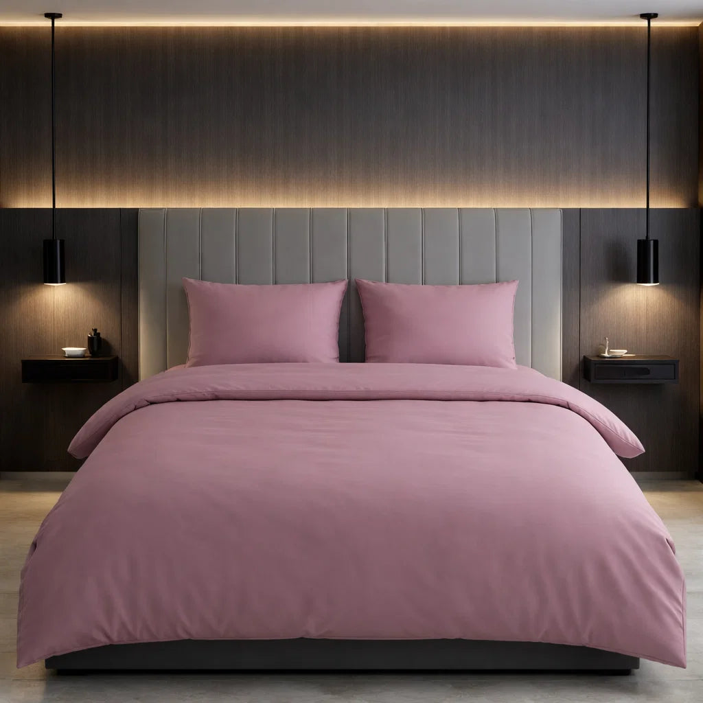 Een moderne slaapkamer met het Decoware dekbedovertrek uni in roze katoen, bijpassende kussens en wandlampen op donkere muren.